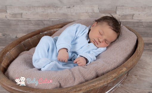 Säugling schläft in einer Holzschale auf weicher Decke – Neugeborenenfotografie.