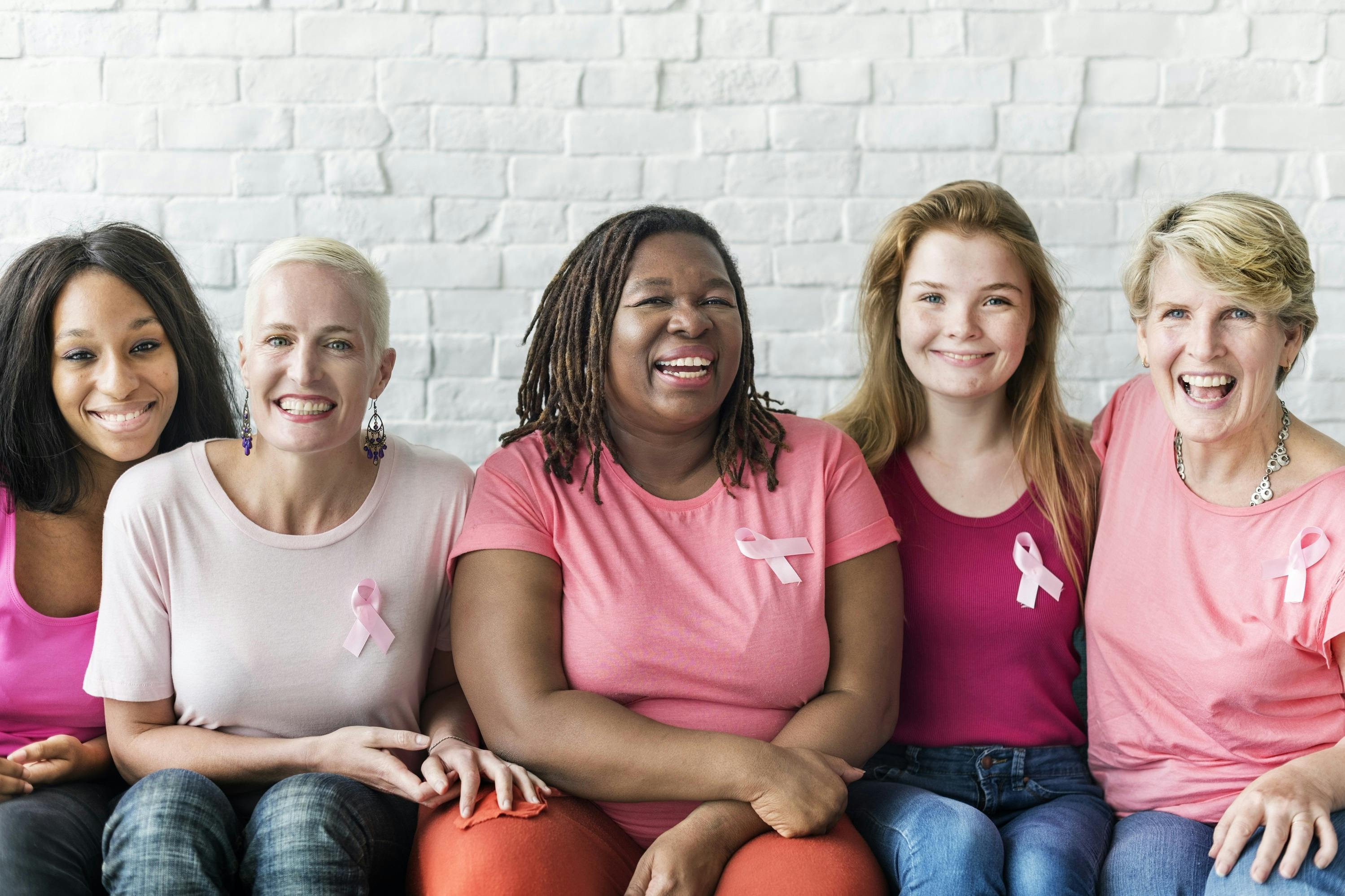 Mehrere lächelnde Frauen mit einer pinken Brustkrebsschleife sitzen nebeneinander
