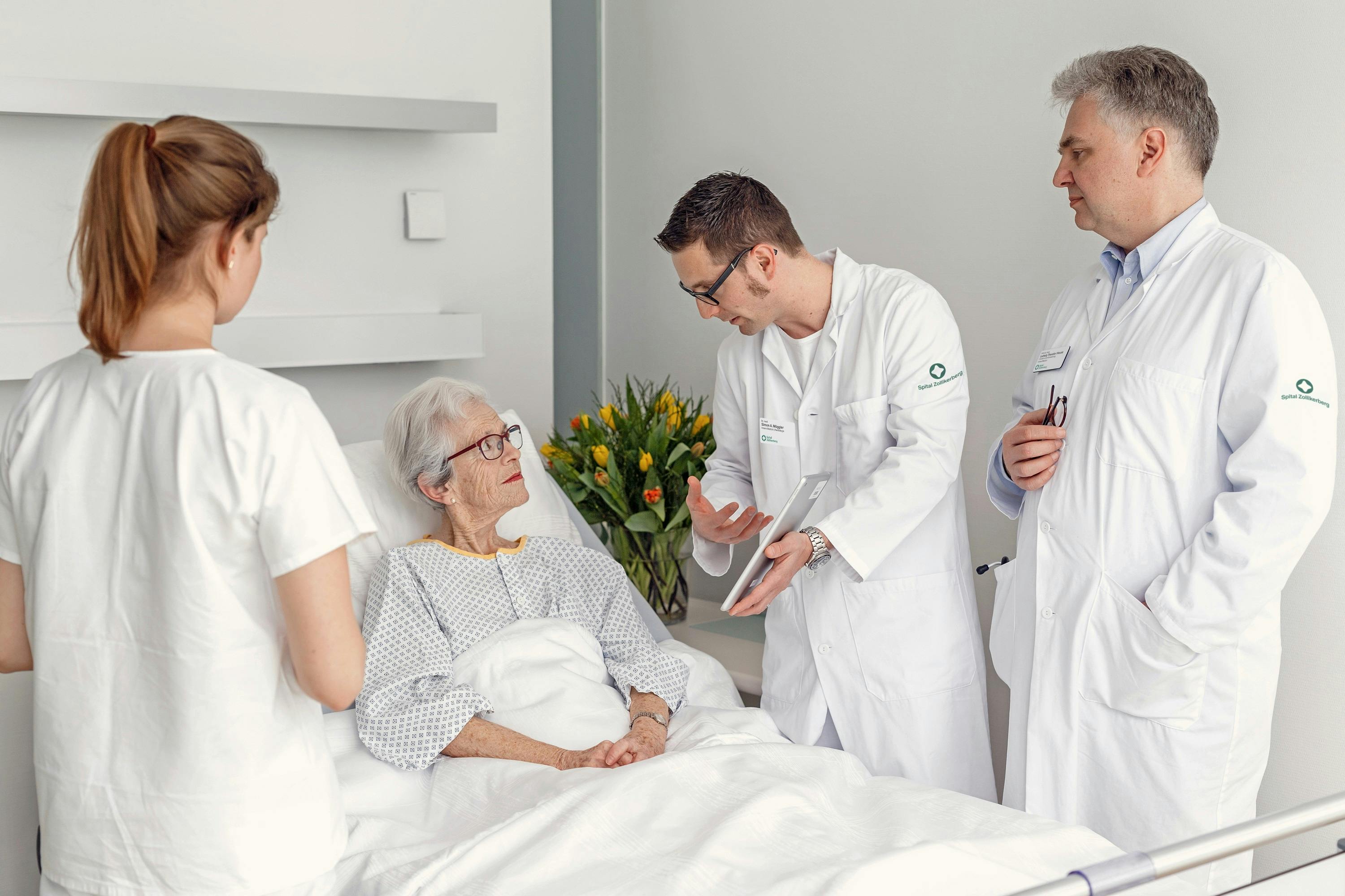 Senior citizen in hospital bed talks to medical team.