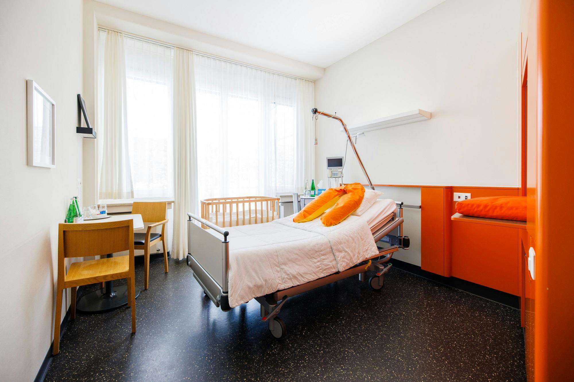 Krankenhauszimmer mit Bett, Nachttisch und Fenster.