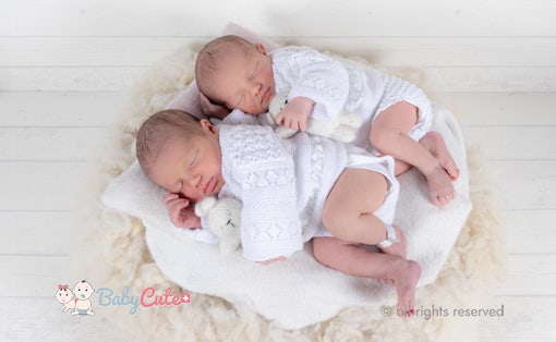 Zwillinge schlafen friedlich nebeneinander auf einer weißen Decke, eingehüllt in gestrickte Kleidung.