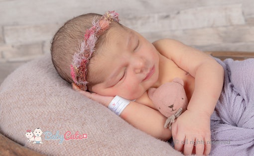 Neugeborenes mit Stirnband schläft mit Kuscheltier.