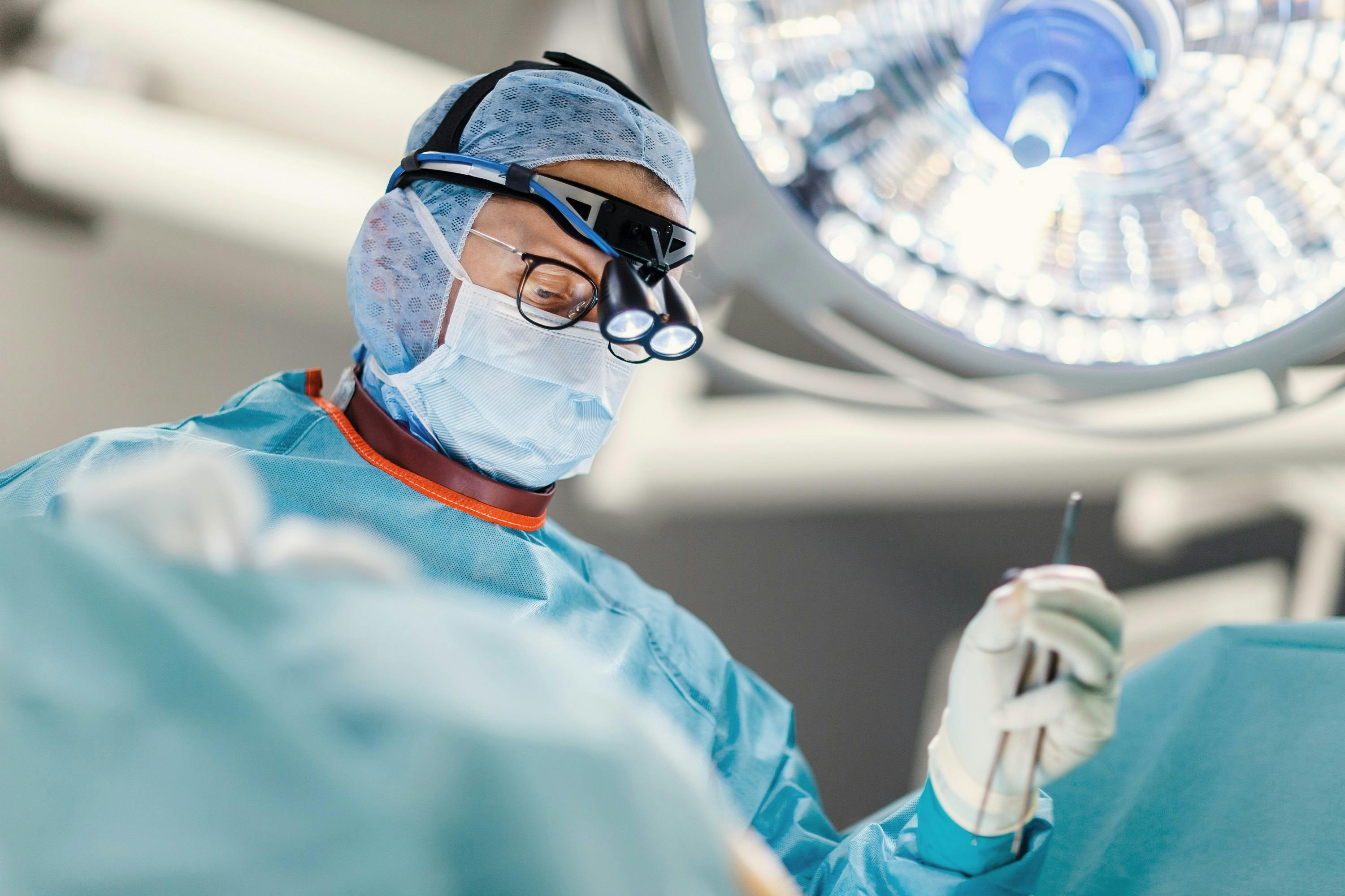Chirurg in Operationskleidung und mit Lupenbrille bei der Arbeit im OP-Saal.