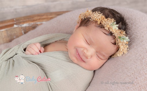 Smiling baby with a wreath of flowers, wrapped in a green blanket.