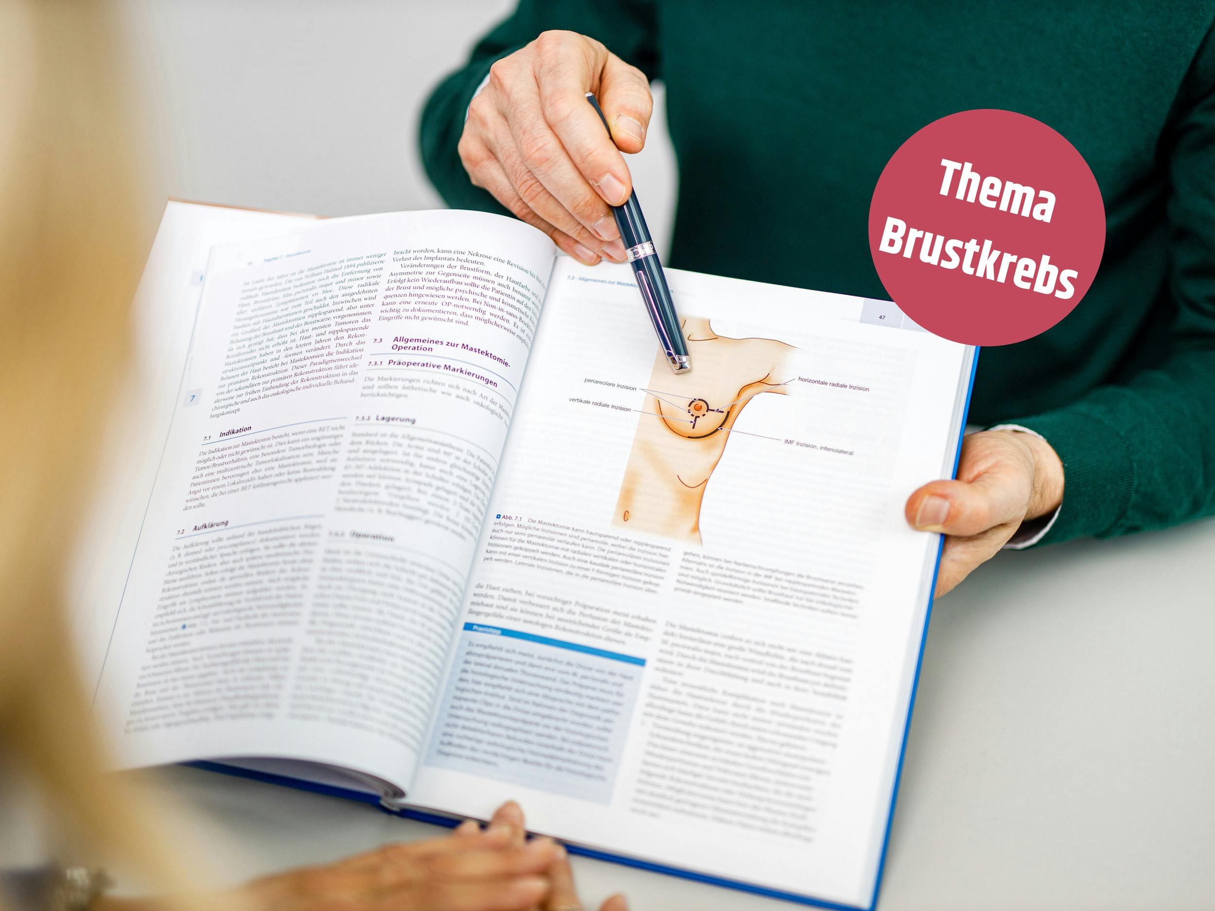 Person hält Stift an eine medizinische Abbildung im Lehrbuch mit Thema Brustkrebs.