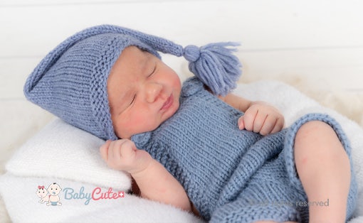 Newborn baby in blue knitted hat and blanket sleeps peacefully.