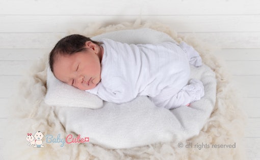 Neugeborenes schläft friedlich eingewickelt in weißer Decke.