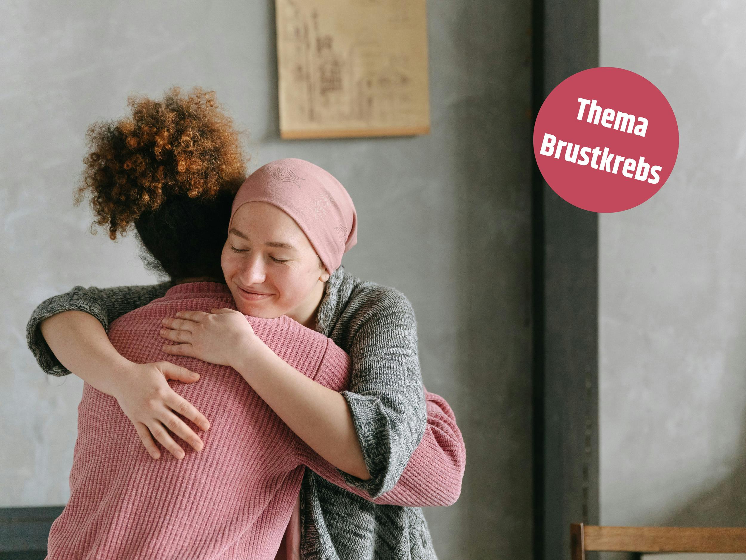Zwei Frauen umarmen sich herzlich, eine davon trägt ein Kopftuch, thematisches Icon mit dem Wort 'Brustkrebs' in der Ecke.