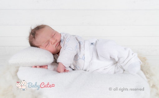Neugeborenes schläft auf weicher Decke, weißes Outfit, Bild mit Urheberrechtsvermerk "BabyCute".