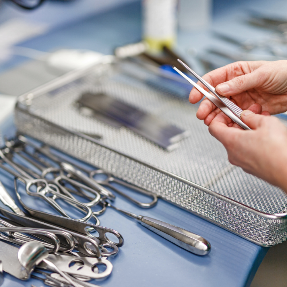 Surgical instruments on a table with a hand holding tweezers.