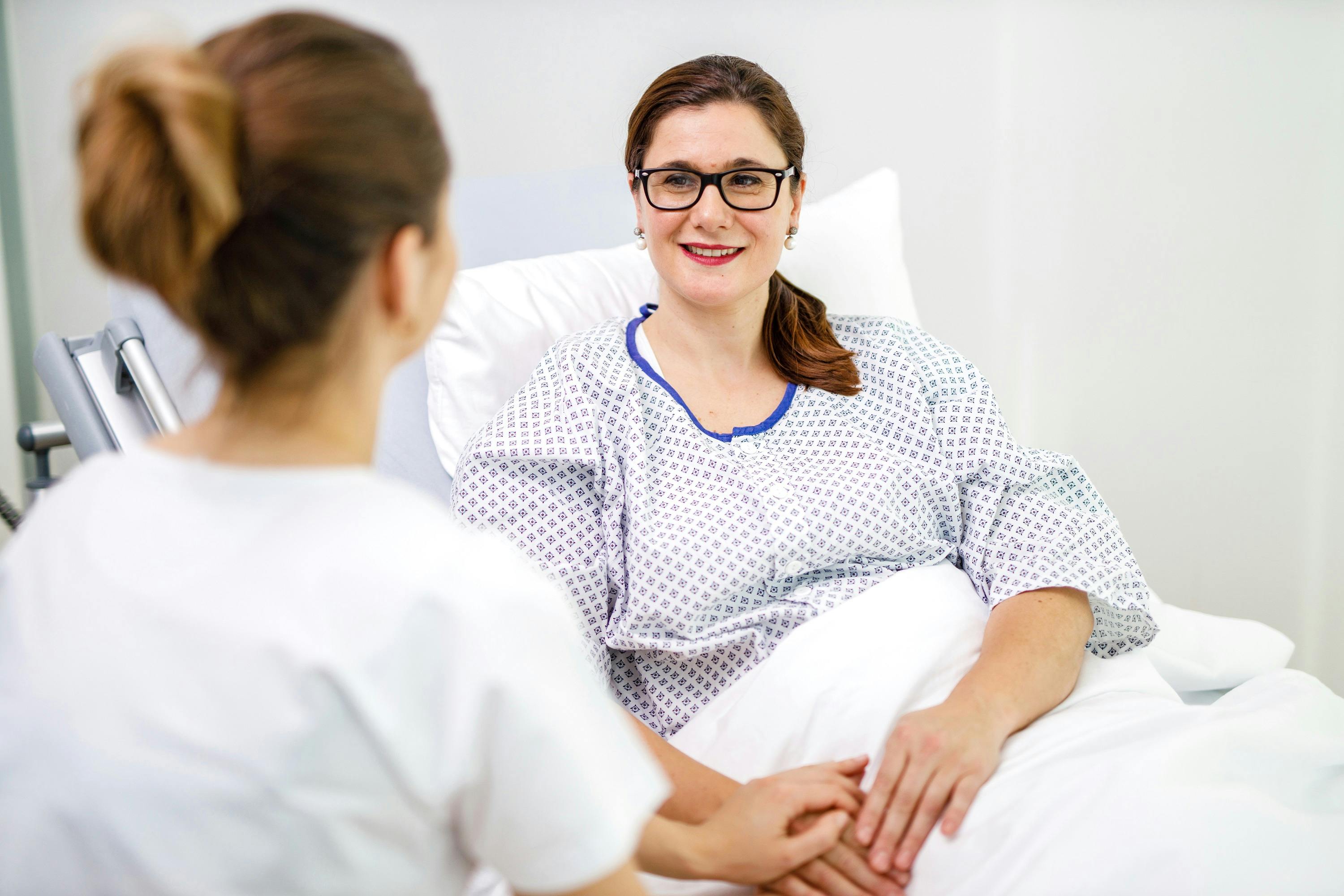 Woman in hospital gown smiles at healthcare staff.