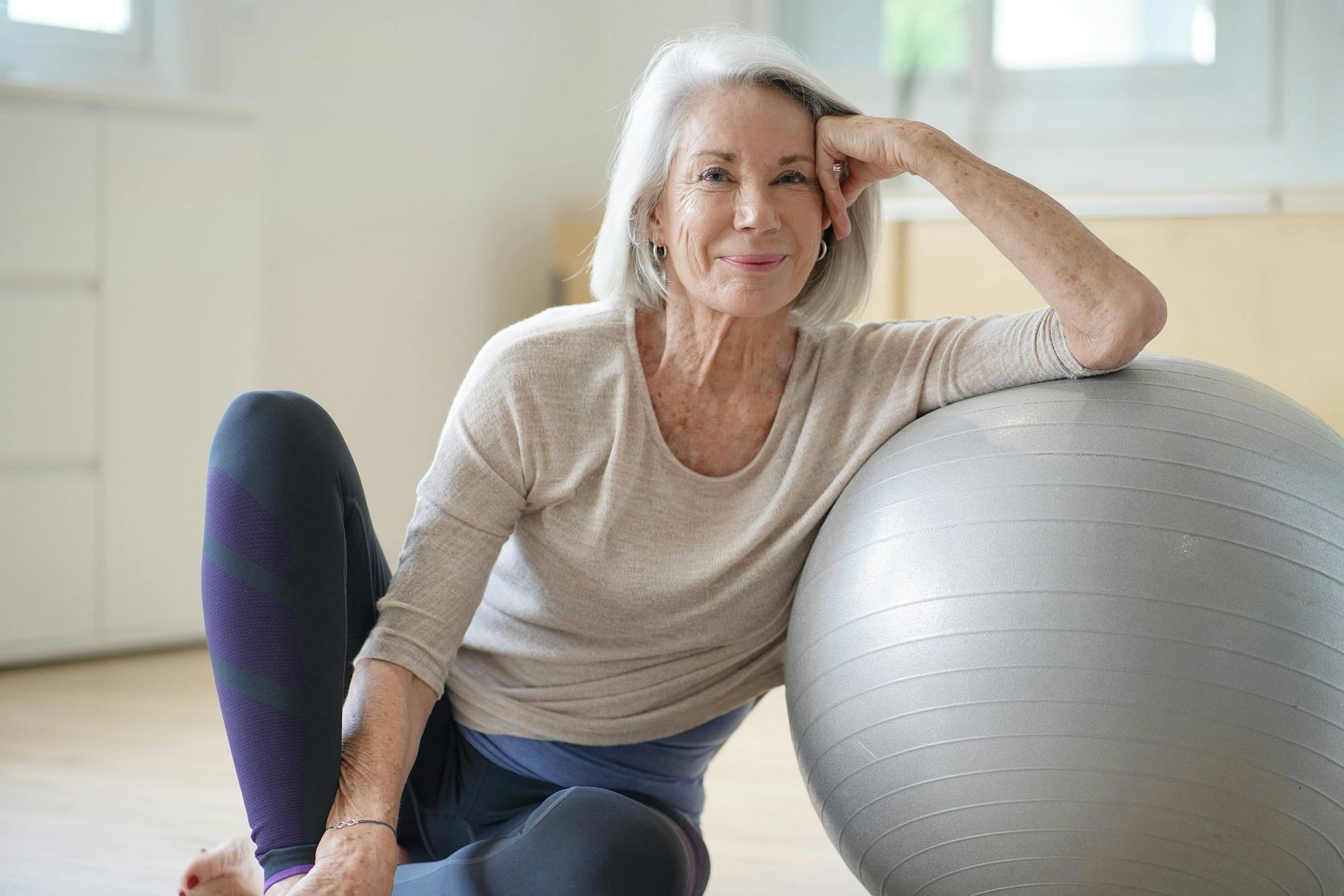 Older woman smiles during fitness training with exercise ball.