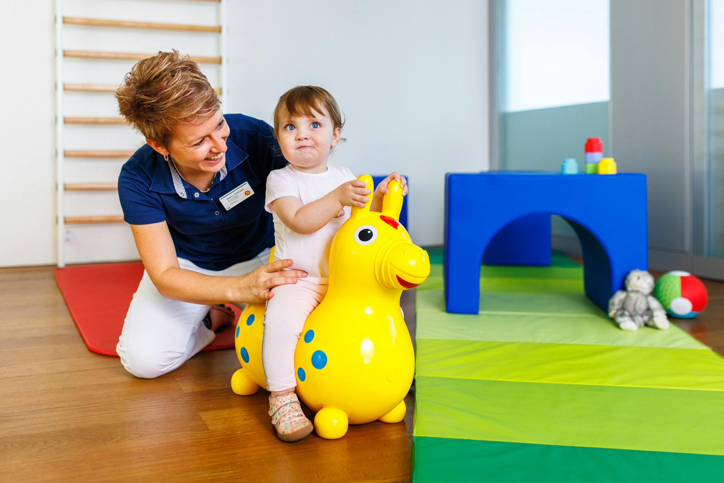 Kleinkind auf einem gelben Hüpftier mit Betreuerin bei Kinderphysio Spital Zollikerberg.