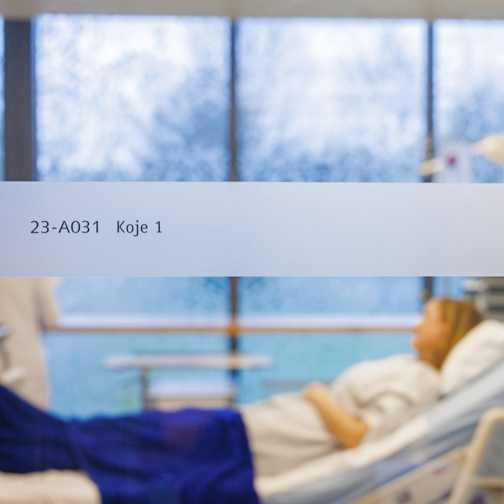 Patientin im Krankenhausbett mit Blick auf verschneites Fenster, Zimmer 23-A031 Koje 1.