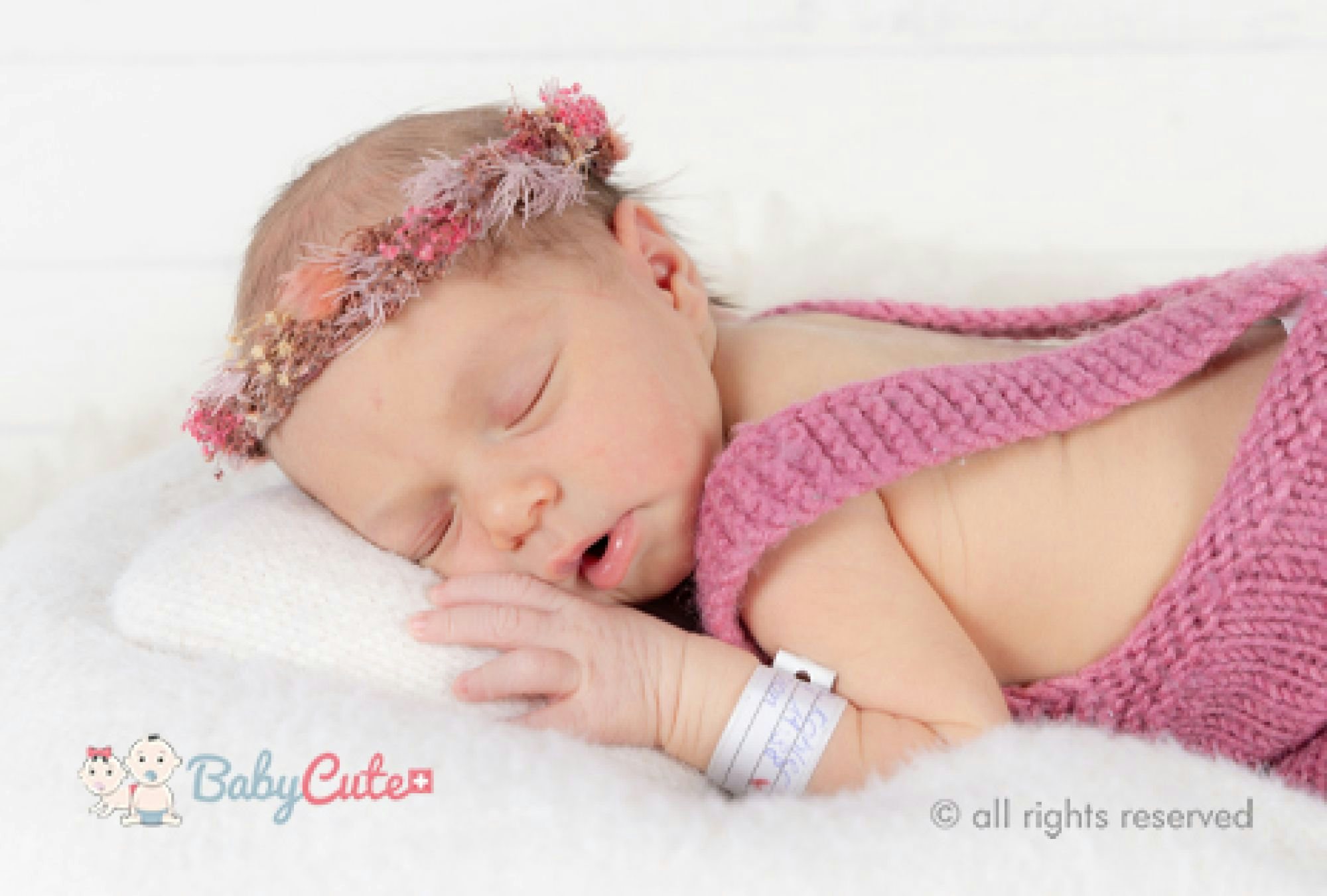 Neugeborenes schläft mit Blumenhaarband und rosa Strickdecke.