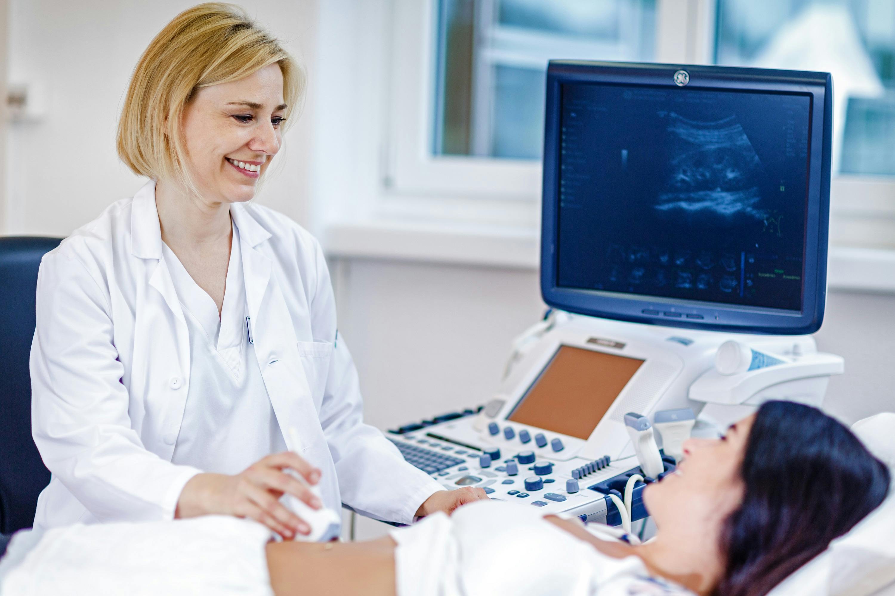 Lächelnde Ärztin führt Ultraschalluntersuchung bei schwangerer Patientin durch.