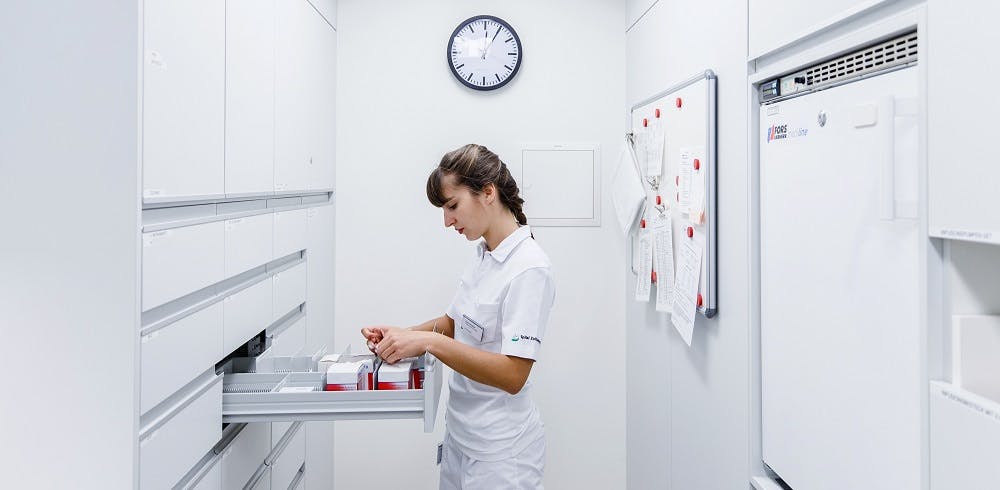 Nurse prepares medication in a white, tidy treatment room.