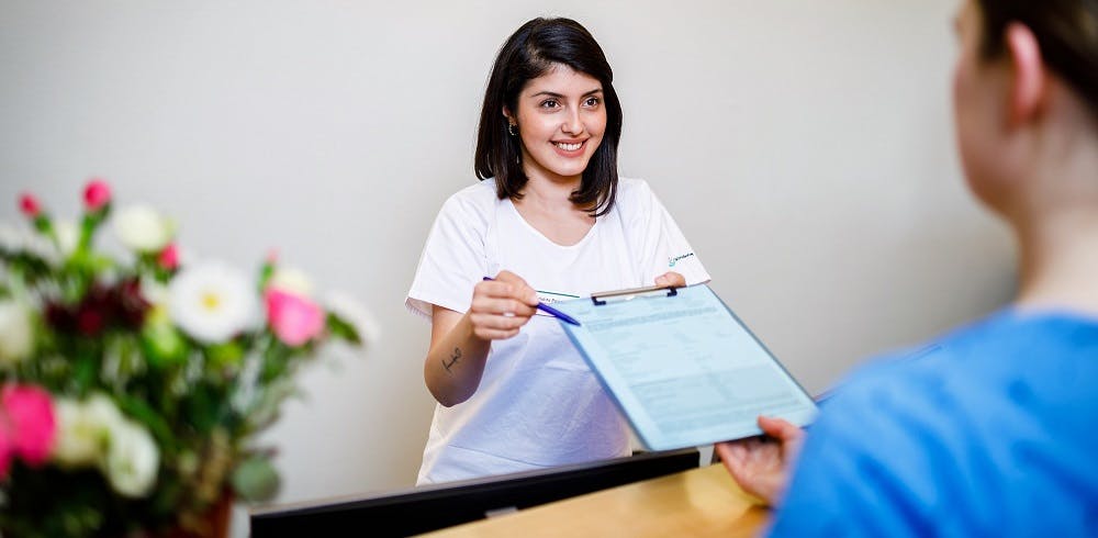 Smiling woman hands over document and pen for signature.