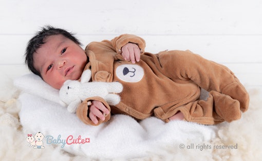 Infant in a bear costume holding a soft toy.