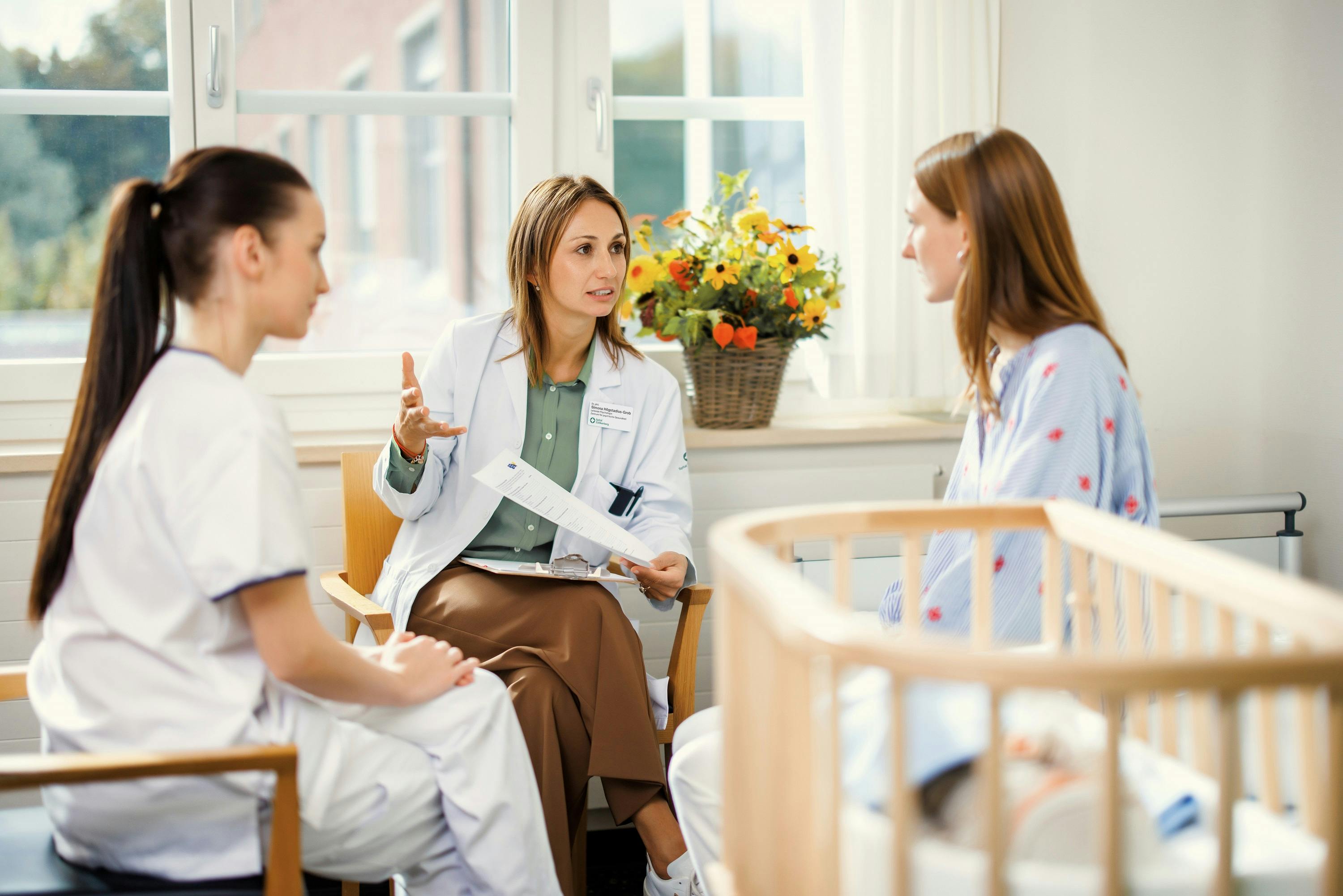 Ärztin im Gespräch mit Patientin und Krankenpflegerin in einem Krankenhauszimmer.