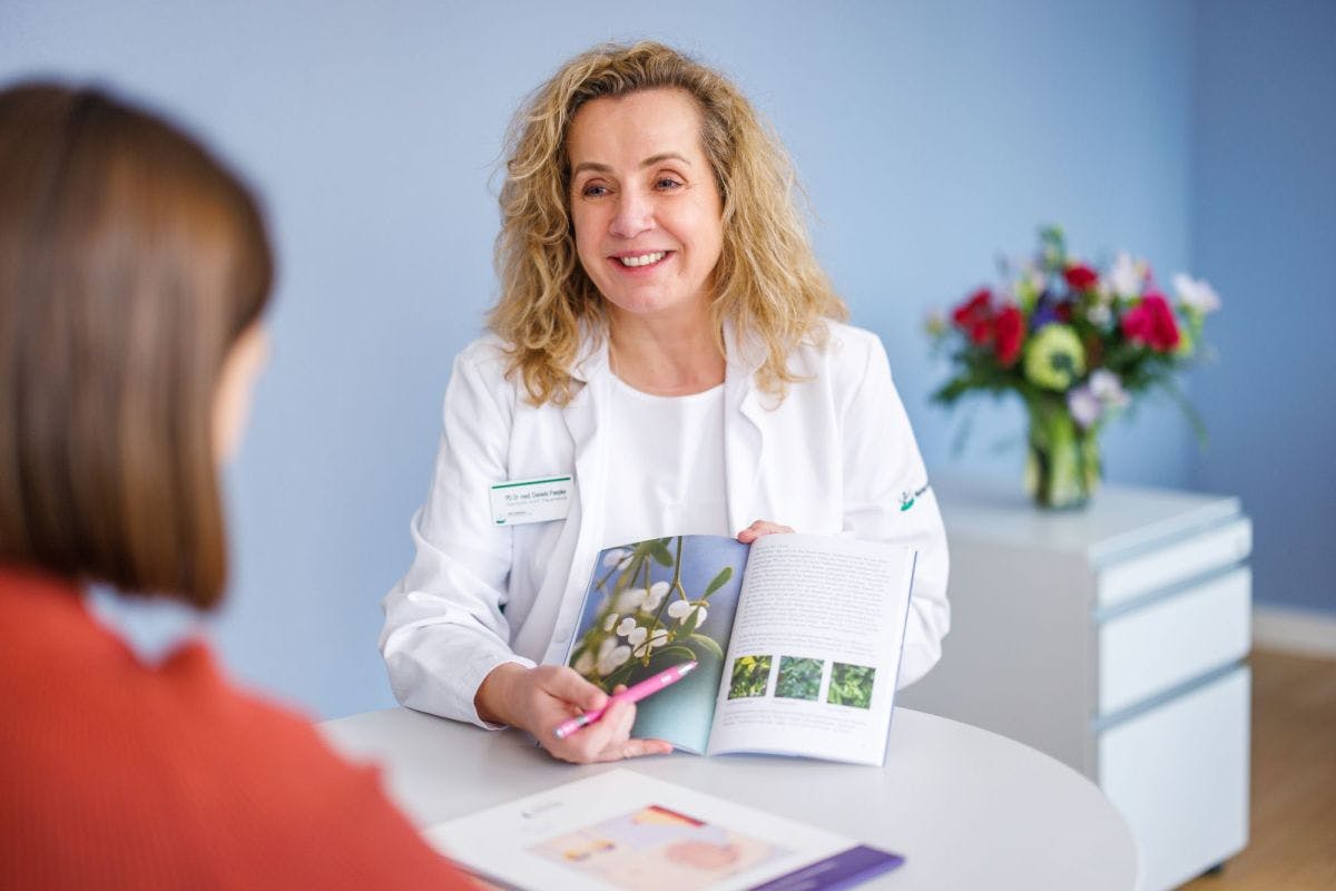 Doctor in white coat advises patient with information brochure in brightly lit practice.