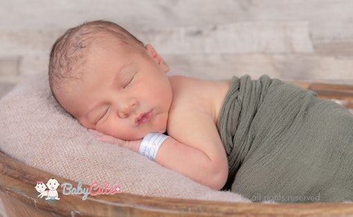 Newborn baby sleeping wrapped in a green blanket.