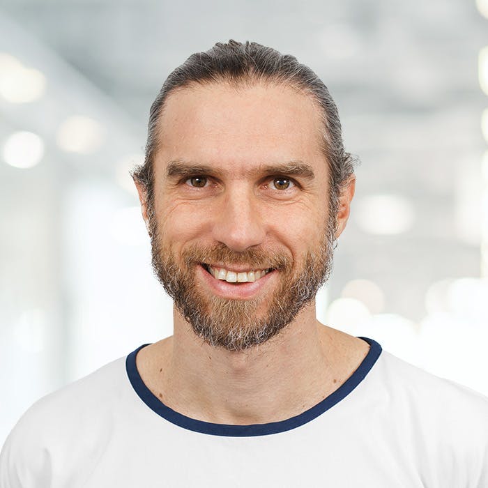 Lächelnder Mann mit Bart und T-Shirt vor unscharfem Hintergrund.