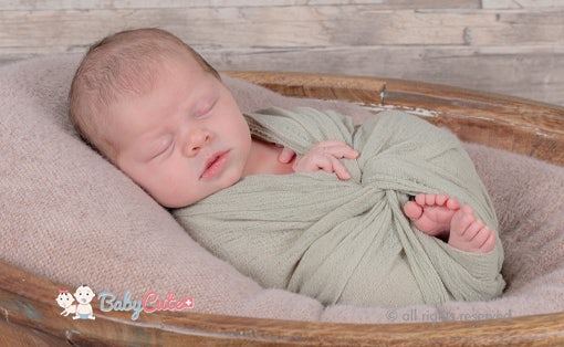 Sleeping newborn baby wrapped in green cloth, lying in a basket.