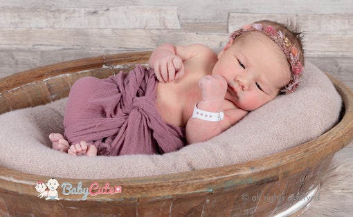 Neugeborenes in Holzkorb mit lila Tuch und Haarband.