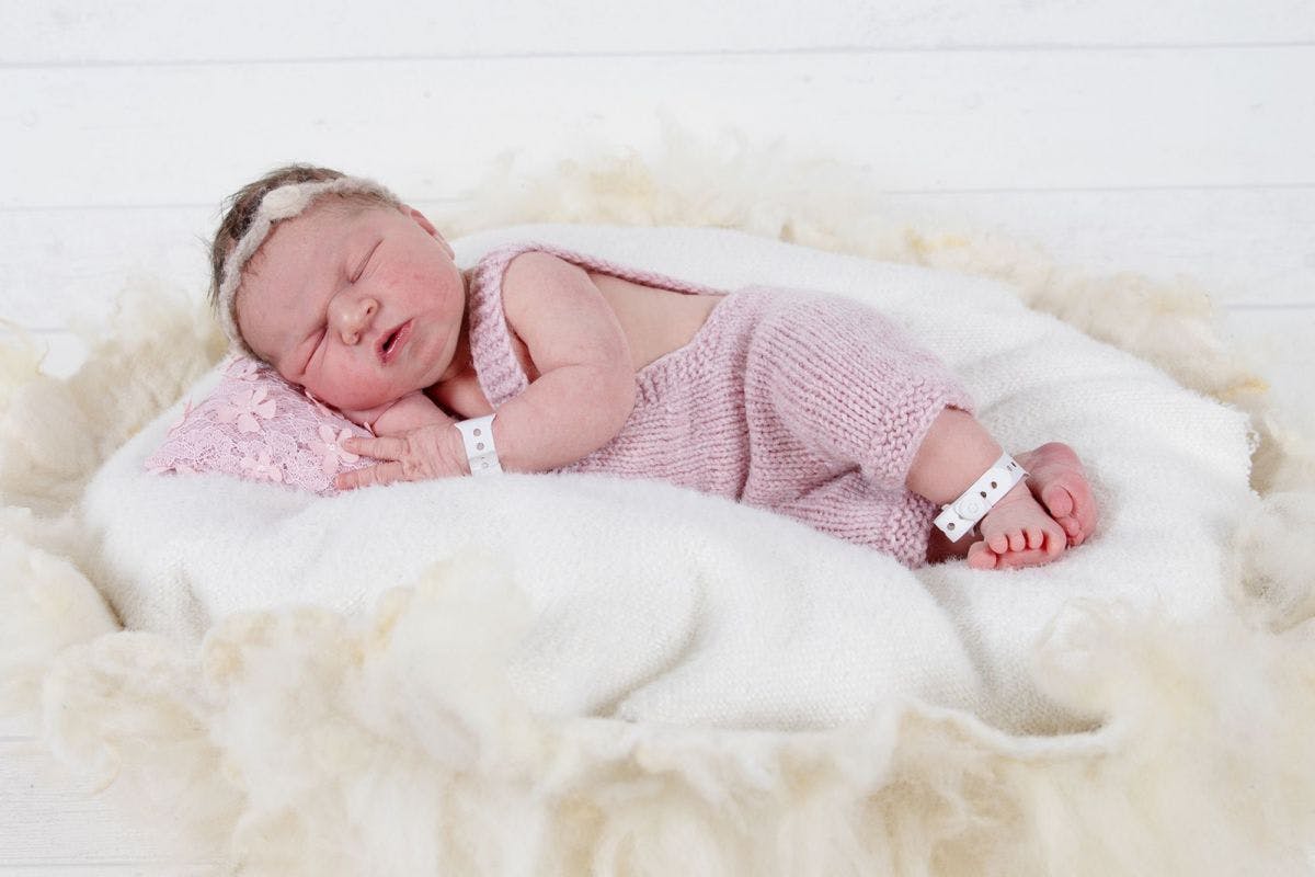 Sleeping newborn baby in pink romper suit on a white blanket.