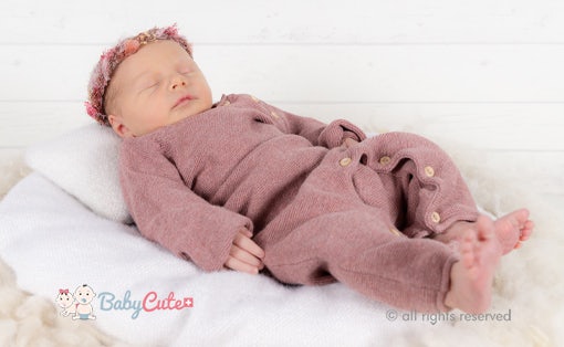 Säugling in rosafarbener Stramplerkleidung schläft auf weißer Decke.