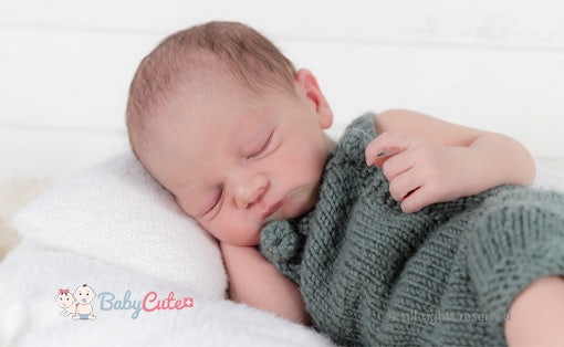Neugeborenes schläft friedlich eingewickelt in einer grauen Decke.