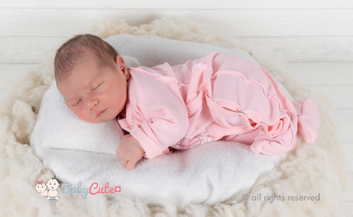 Schlafendes Neugeborenes in rosa Strampler auf weißer Decke.