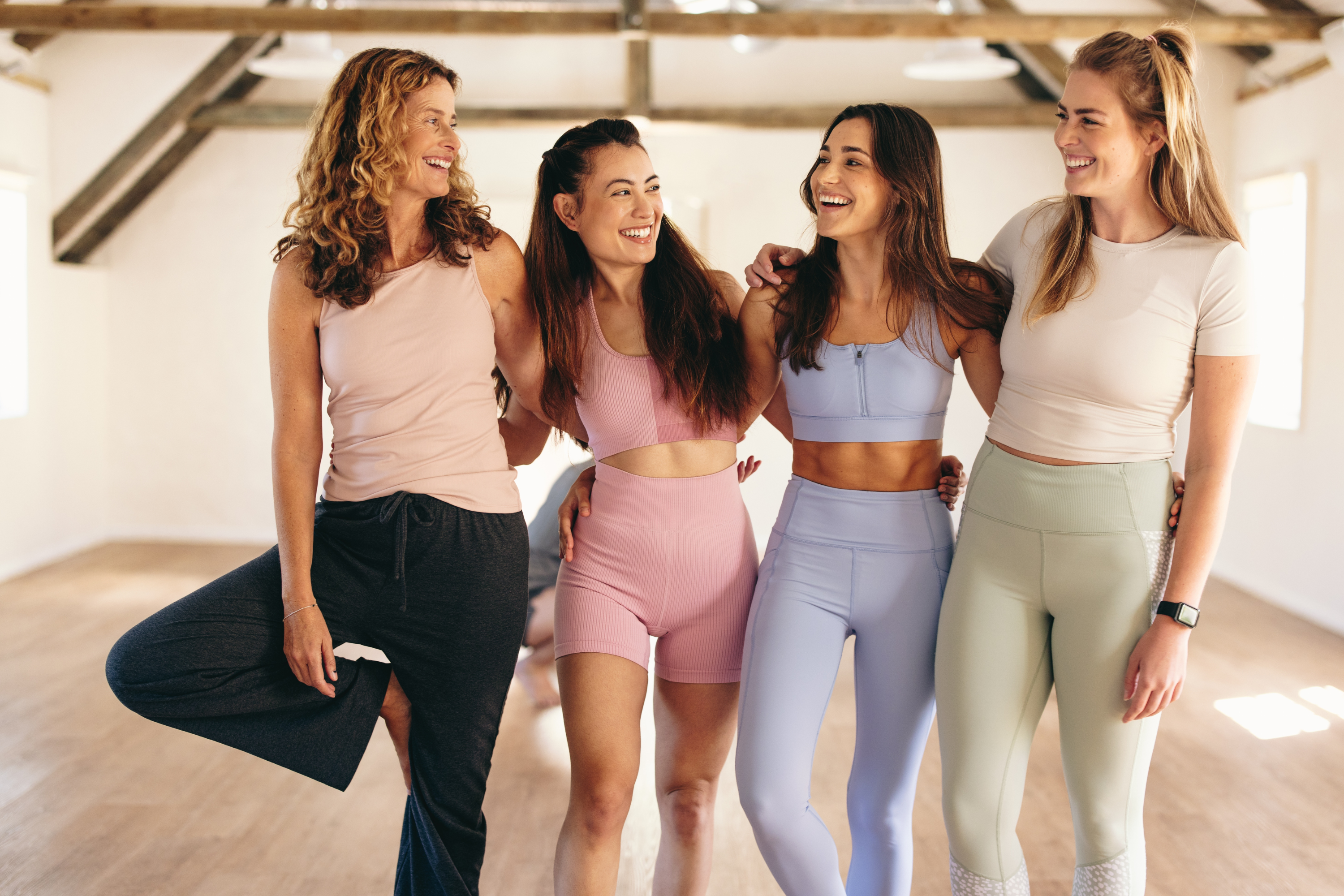 Four women in sportswear smile and stand together.