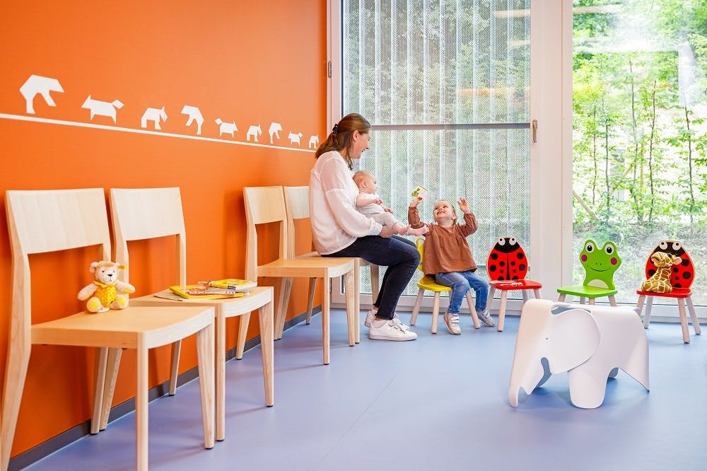 Woman with a baby on her lap and toddler in a colourful playroom.