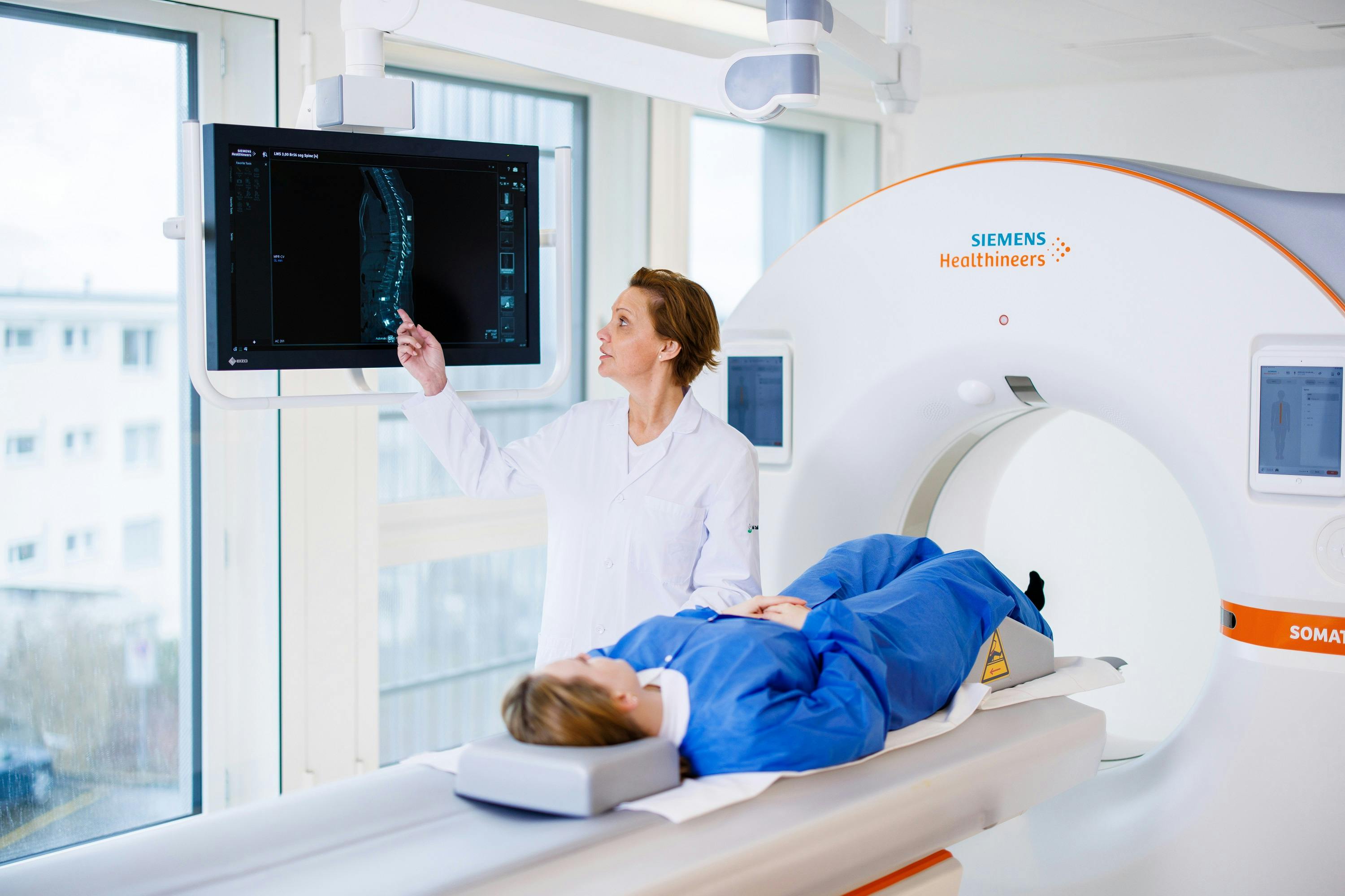 Medical specialist looks at X-ray image next to patient in MRI machine from Siemens Healthineers.