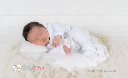 Schlafendes Neugeborenes in weißer Kleidung auf einer weichen Unterlage.