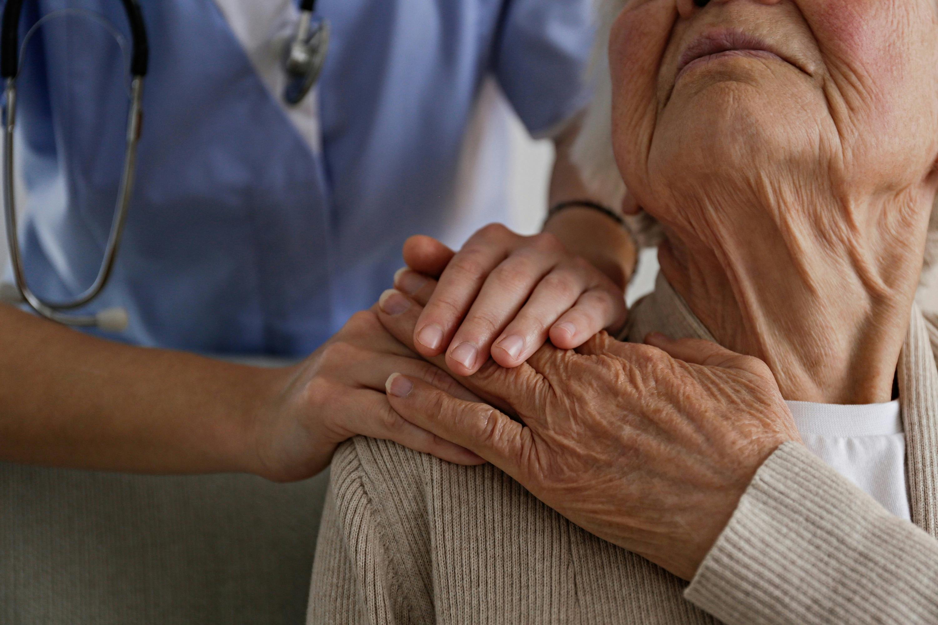 Pflegerin legt ihre Hände auf die Schulter der älteren Patientin, die zu ihr hochsieht. 