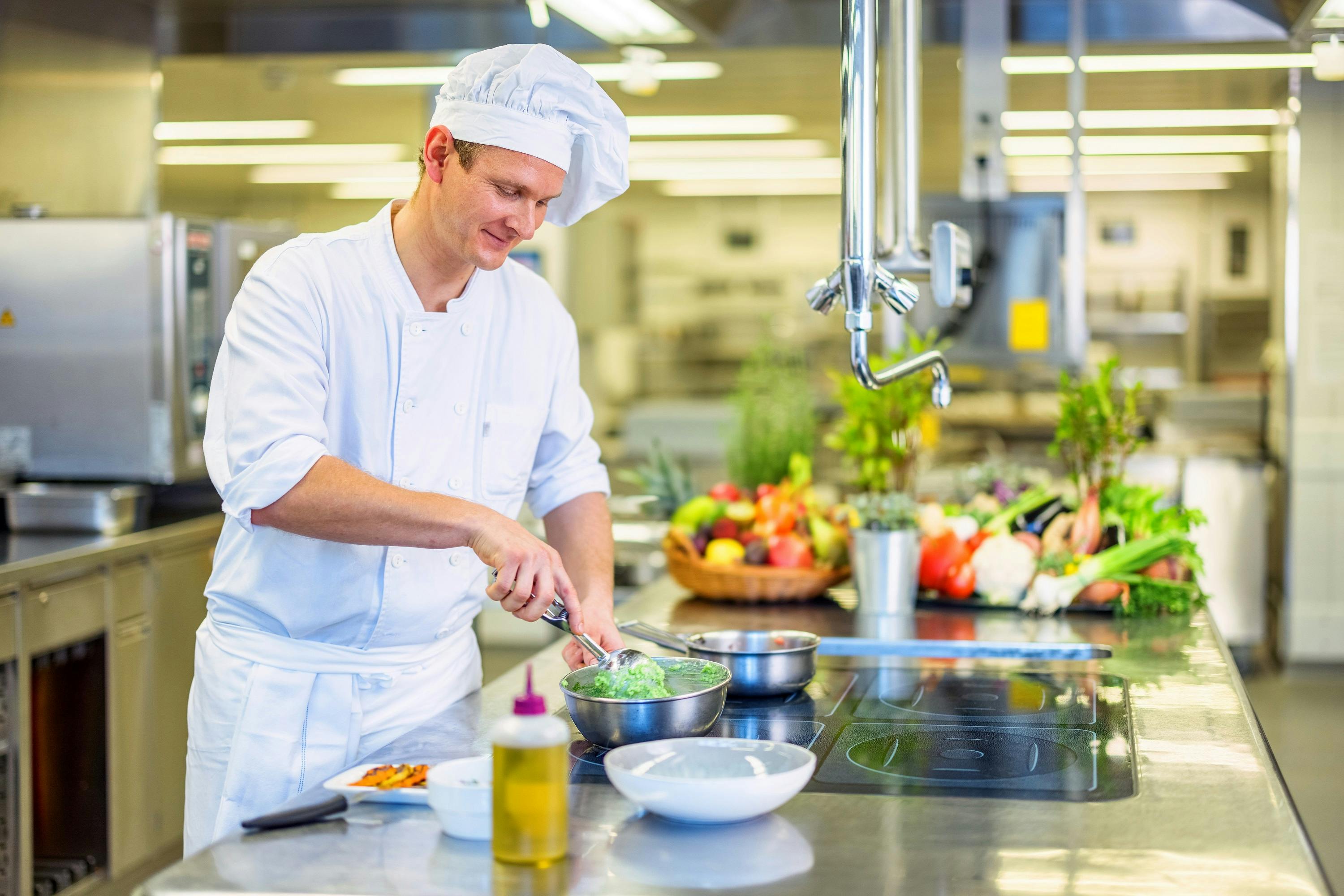 Cook in white uniform prepares food in a professional kitchen.